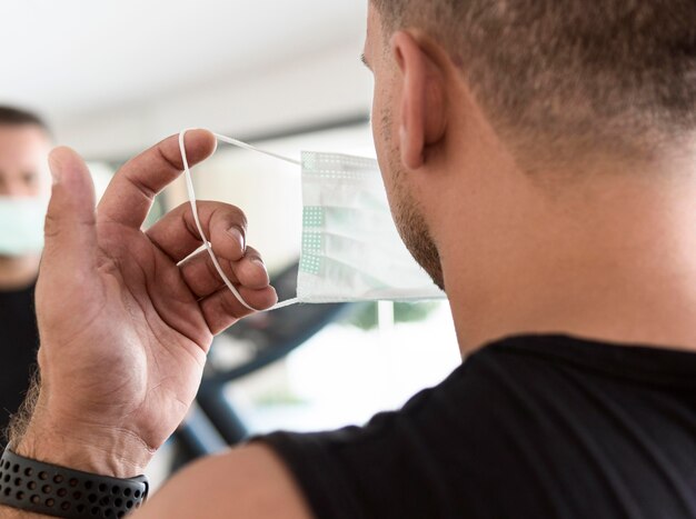 Vista posterior del hombre poniéndose máscara médica en el gimnasio