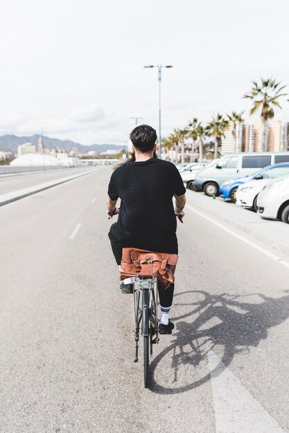 Vista posterior de un hombre que monta la bicicleta en camino recto