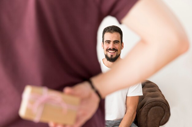 Vista posterior del hombre que oculta la caja de regalo envuelta de su amigo sonriente
