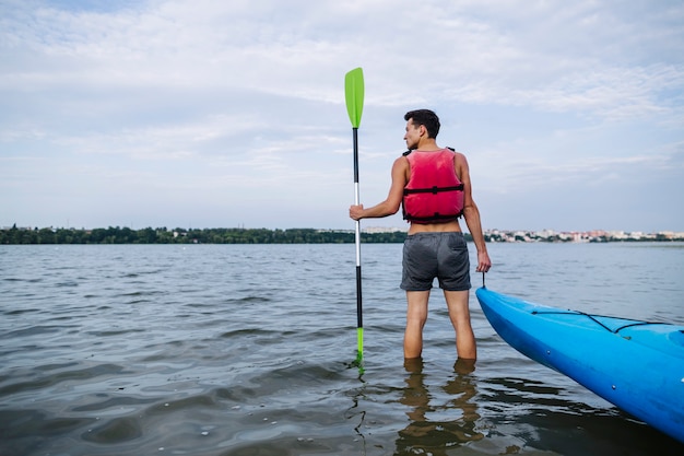 Vista posterior del hombre que sostiene el remo y el kayak de pie en el lago