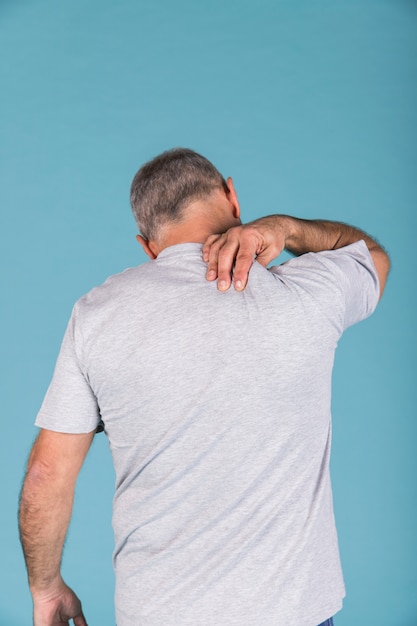 Vista posterior de un hombre que sufre de dolor de cuello frente a un fondo azul