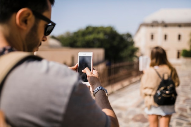 Vista posterior del hombre que toma la fotografía de una mujer mirando el mapa que está parado en la calle