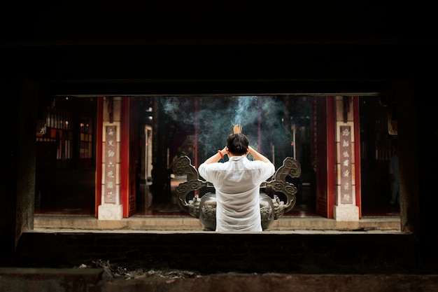 Vista posterior del hombre rezando en el templo con incienso ardiente