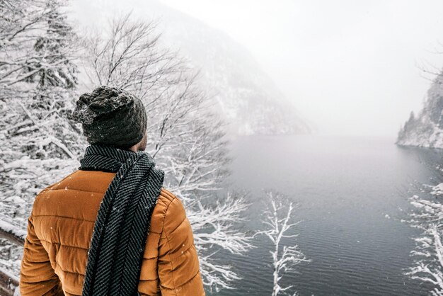 Vista posterior de un hombre en ropa de invierno disfrutando del invierno brumoso cerca de un río de montaña