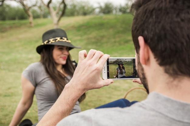 Foto gratuita vista posterior de un hombre tomando una foto de su novia sentada en el parque