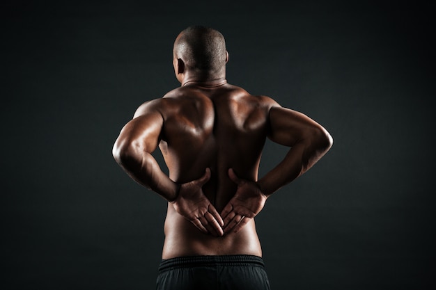 Vista posterior del joven deportista africano siente dolor en la espalda