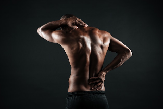 Vista posterior del joven deportista africano siente dolor en la espalda