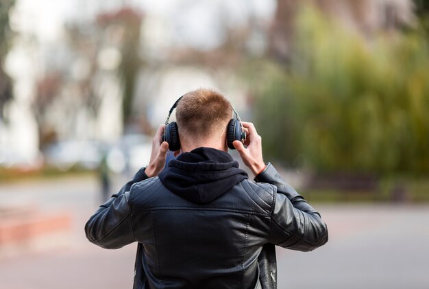 Vista posterior joven escuchando música con auriculares