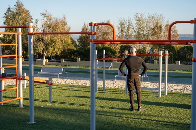 Vista posterior de un joven hispano que descansa después de hacer ejercicio en el campo de deportes