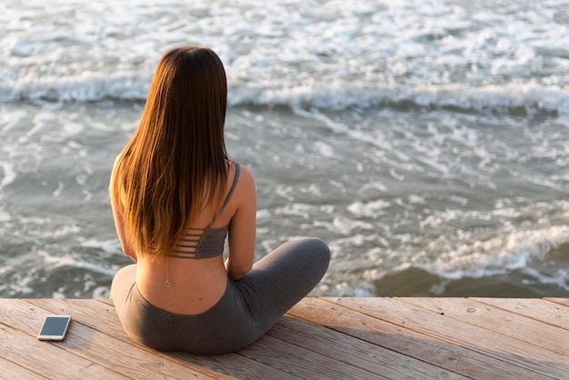 Vista posterior joven meditando junto al mar