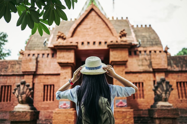 Vista posterior de la joven mujer asiática mochilero con cabello largo negro con sombrero de pie hormiga mirando al hermoso sitio antiguo o al templo antiguo durante el viaje de vacaciones