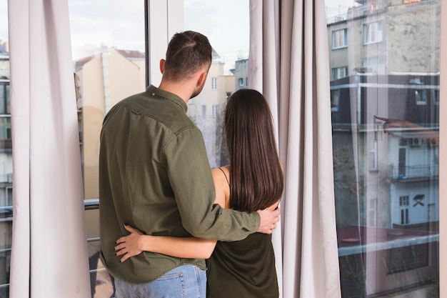 Vista posterior de la joven pareja abrazándose mirando por la ventana