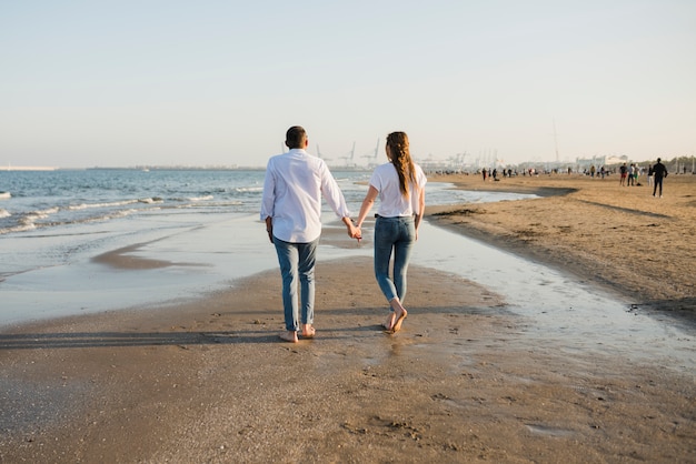 Vista posterior de una joven pareja caminando cerca de la costa en la playa