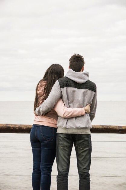 Vista posterior de la joven pareja de pie cerca de la barandilla con vistas al mar