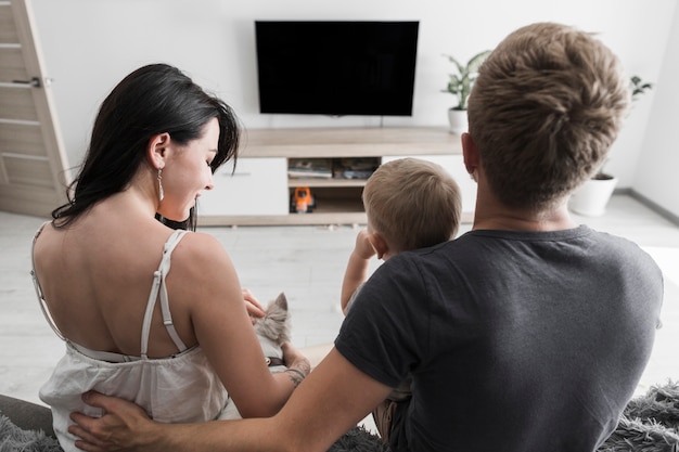 Vista posterior de la joven pareja sentada con su perro y su bebé viendo la televisión