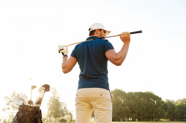 Vista posterior de un jugador de golf masculino en el campo con un saco de palos