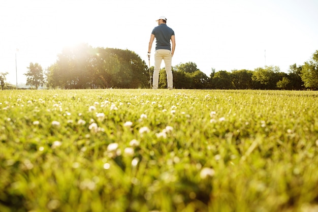 Vista posterior de un jugador de golf masculino en el campo verde con un palo