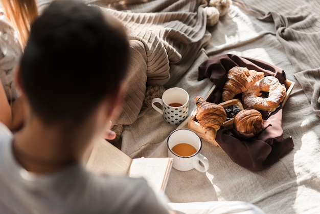 Foto gratuita vista posterior de un libro de lectura de hombre con desayuno en la cama