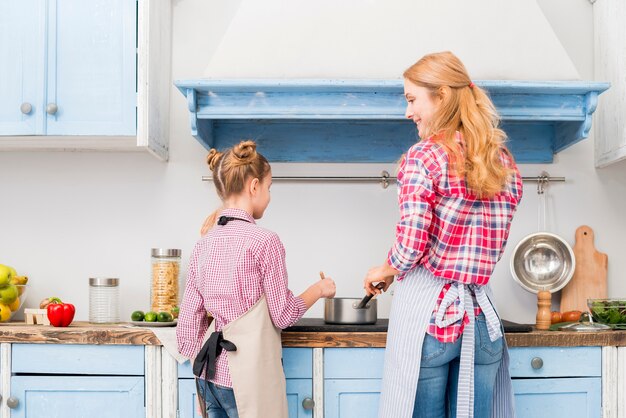 Vista posterior de la madre y su hija cocinando comida en la cocina.