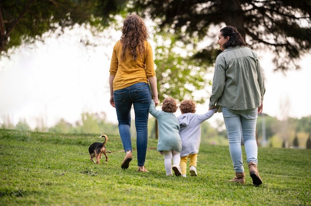 Vista posterior de madres lgbt afuera en el parque con sus hijos y su perro.