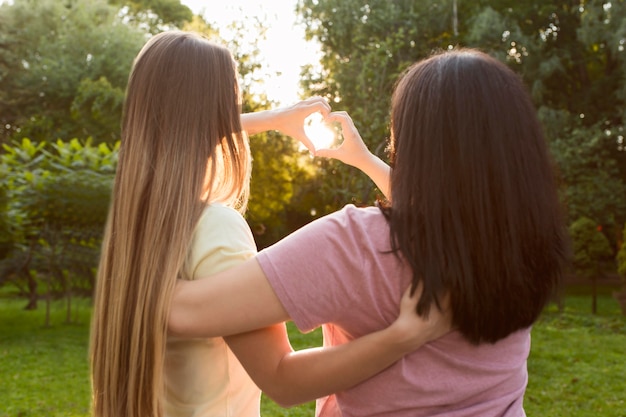 Vista posterior mejores amigos haciendo un corazón en la luz del sol