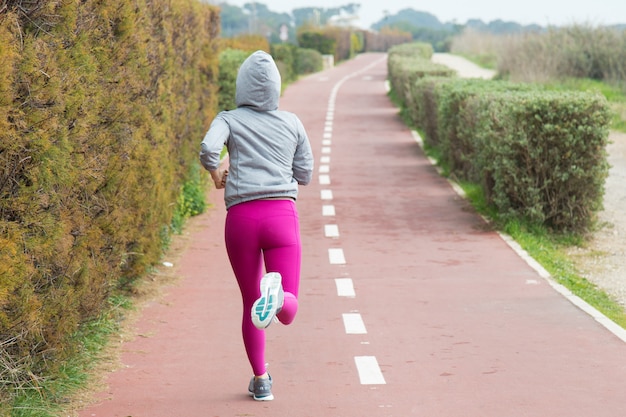 Vista posterior de la mujer deportiva en las polainas rosadas que se ejecutan sobre la pista