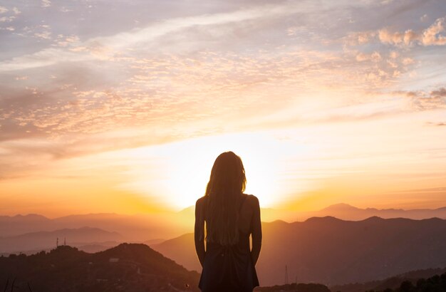 Vista posterior de la mujer haciendo yoga mientras ve la puesta de sol