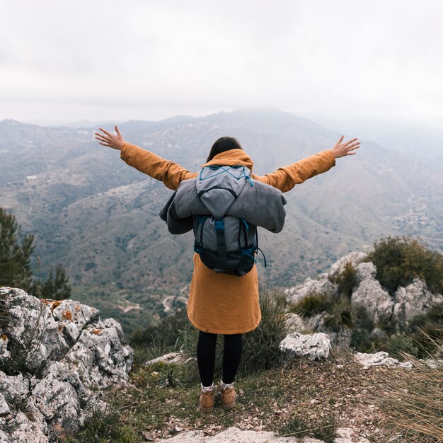 Vista posterior de una mujer joven que estira su mano con la mochila que mira la vista