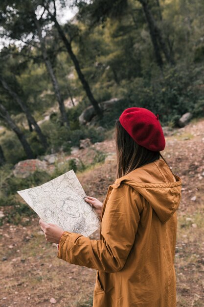 Vista posterior de una mujer joven que lee el mapa en el bosque