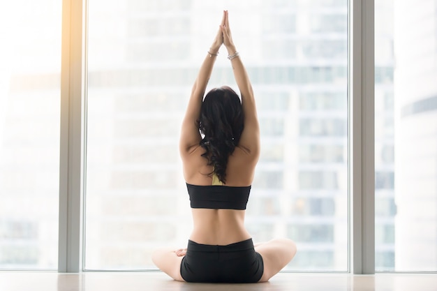 Vista posterior de la mujer joven que se sienta en la actitud de Ardha Padmasana