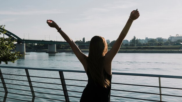 Vista posterior de una mujer levantando sus brazos frente al río