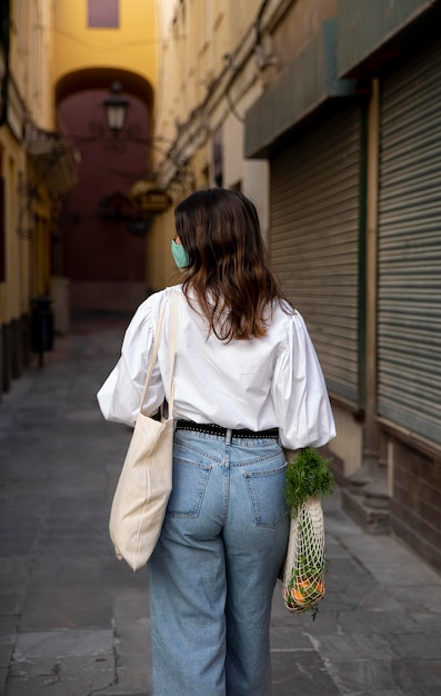 Foto gratuita vista posterior de la mujer con mascarilla y bolsas de la compra.