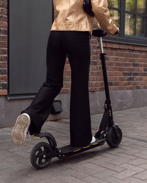 Vista posterior de la mujer montando scooter eléctrico al aire libre