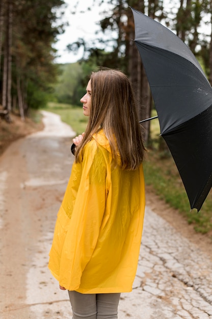 Vista posterior mujer paseando por el bosque mientras sostiene un paraguas