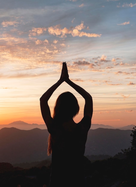 Vista posterior de la mujer en pose de yoga durante la puesta de sol