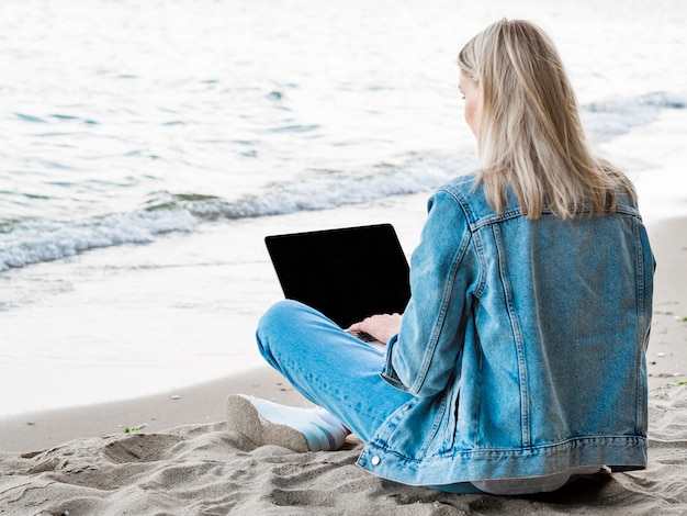 Foto gratuita vista posterior de la mujer que trabaja en la computadora portátil en la playa.