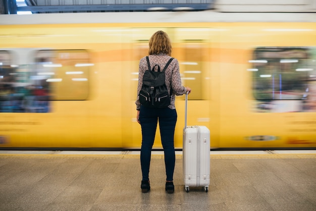 Vista posterior de una mujer rubia esperando en la plataforma del tren