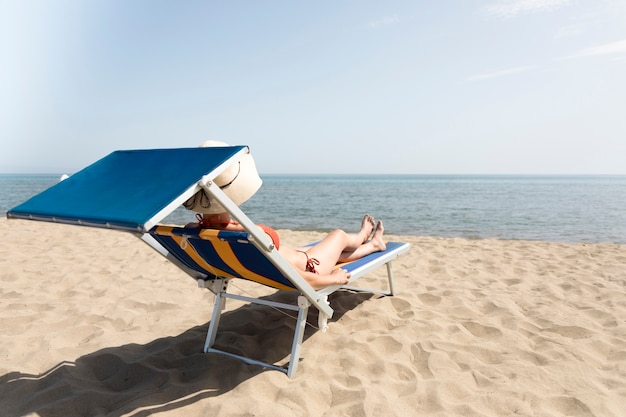 Vista posterior mujer en silla de playa tomando el sol
