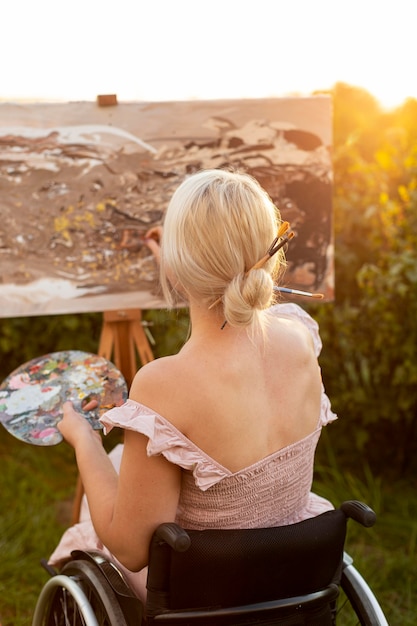 Vista posterior de la mujer en silla de ruedas pintando al aire libre