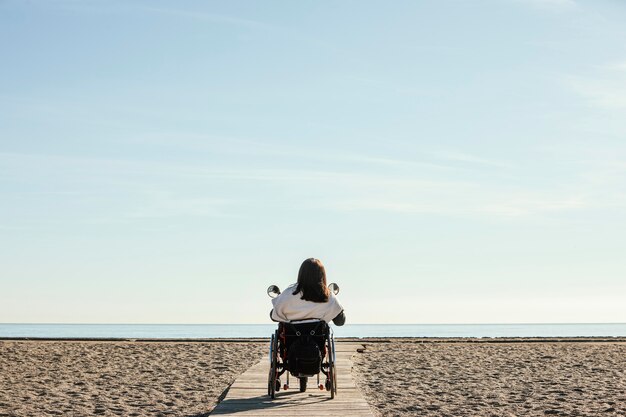 Vista posterior de la mujer en silla de ruedas en la playa.