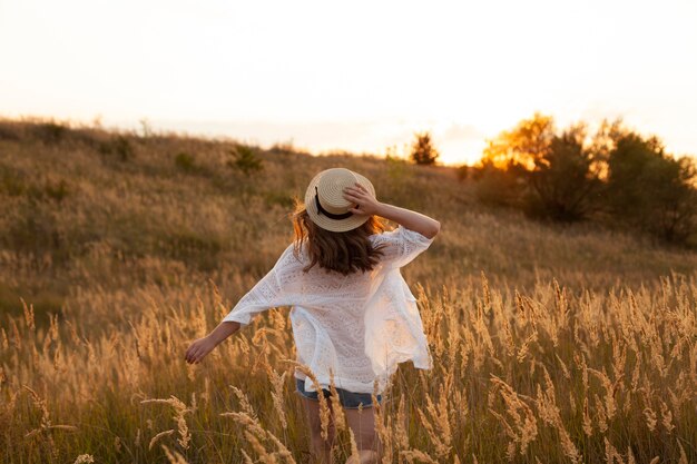 Foto gratuita vista posterior de la mujer con sombrero y posando en los campos