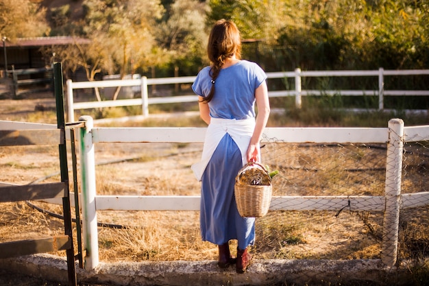 Vista posterior de la mujer sosteniendo la cesta de pie cerca del rancho
