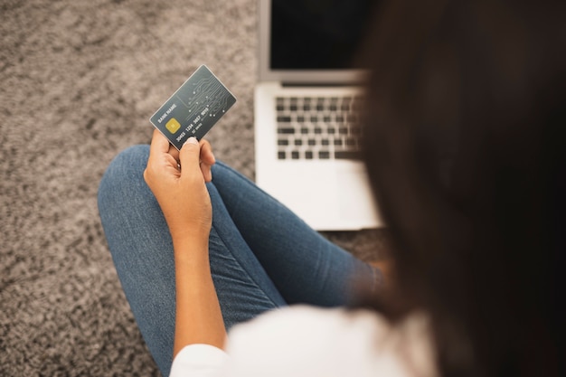 Vista posterior mujer sosteniendo una tarjeta de crédito en el piso