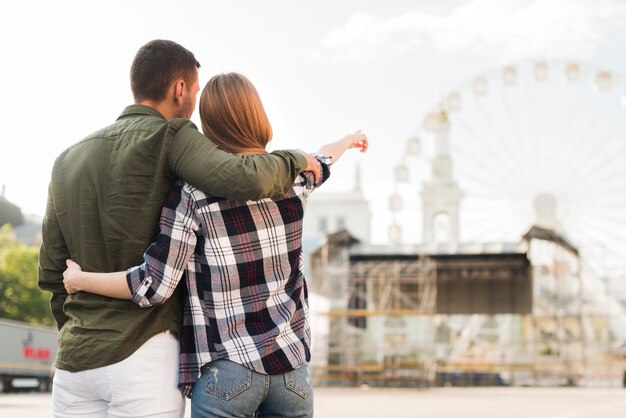 Vista posterior de la mujer con su novio apuntando a la noria mientras