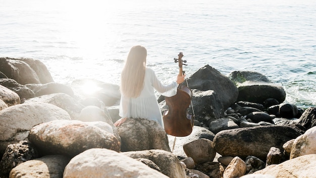 Vista posterior de mujer con violonchelo junto al mar