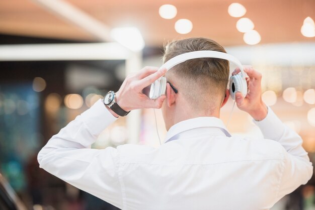 Vista posterior de una música que escucha del hombre joven en el auricular blanco