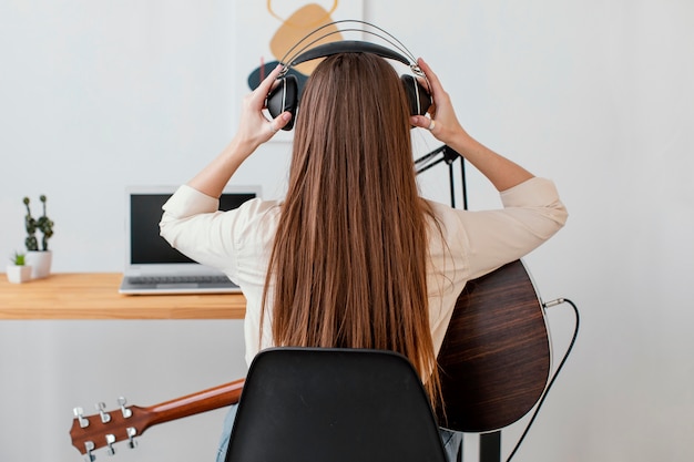 Vista posterior del músico femenino con guitarra acústica y auriculares