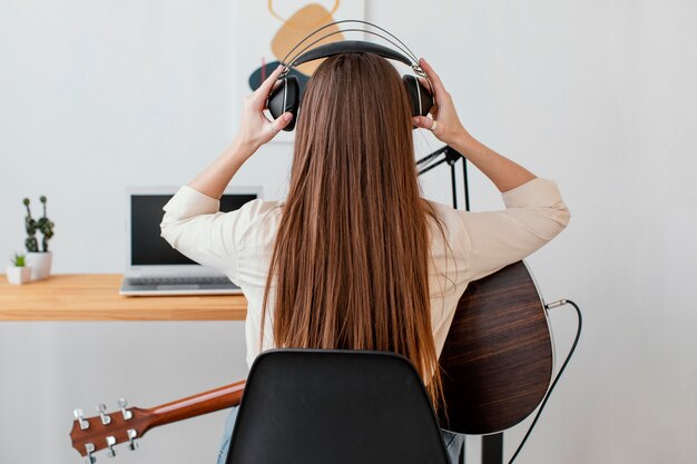 Vista posterior del músico femenino con guitarra acústica y auriculares