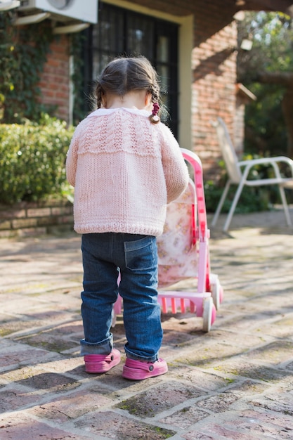 Vista posterior de una niña jugando con cochecito fuera de la casa