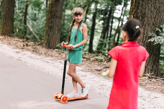 Vista posterior de la niña mirando a su amiga de pie en empuje scooter